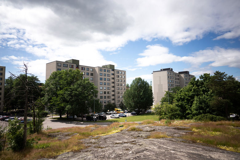 Kerrostalojen edustalla näkyy parkkipaikka ja puita sekä kalliota.