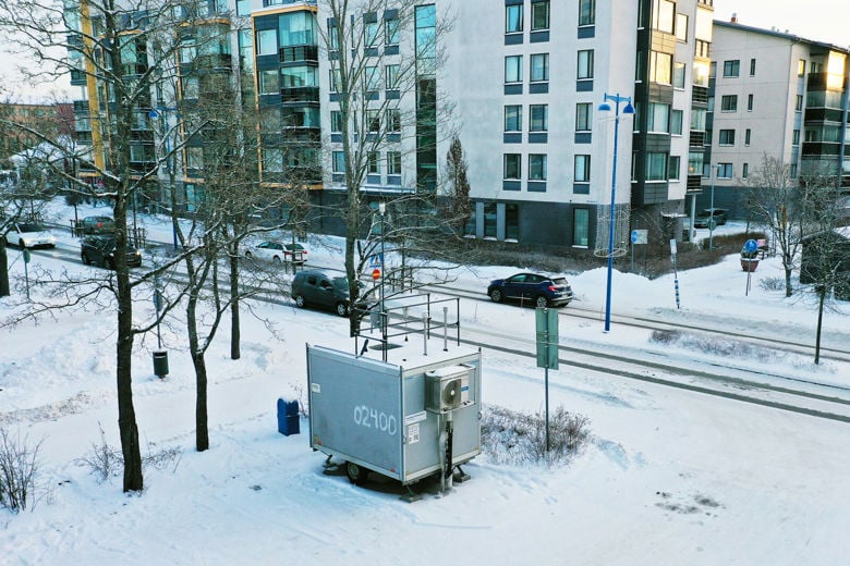 Harmaa mittausasema seisoo kadun varressa.