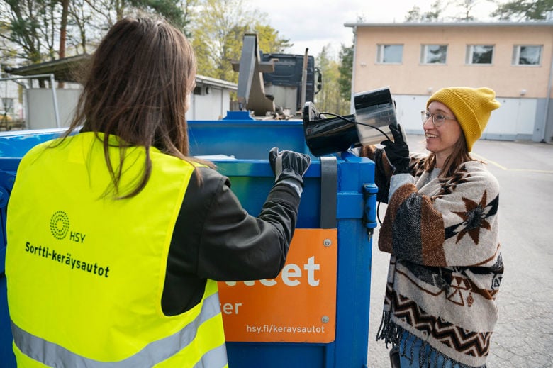 Sortti-keräysautokierroksen asiakas laittaa sähkölaiteromua Sortti-keräysauton lavalle. Keltaiseen huomioliiviin pukeutunut työntekijä on apuna.