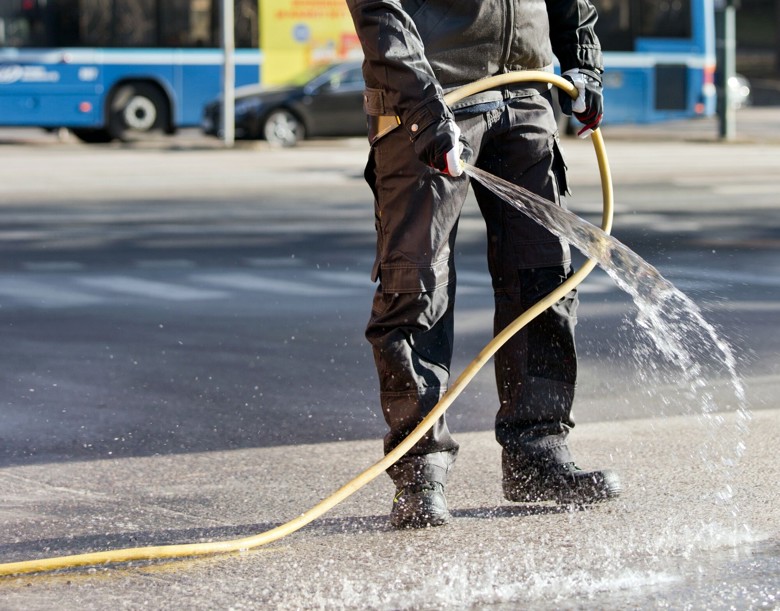 Henkilö kastelee katua letkulla vähentääkseen pölyn muodostumista hiekan poiston aikana.