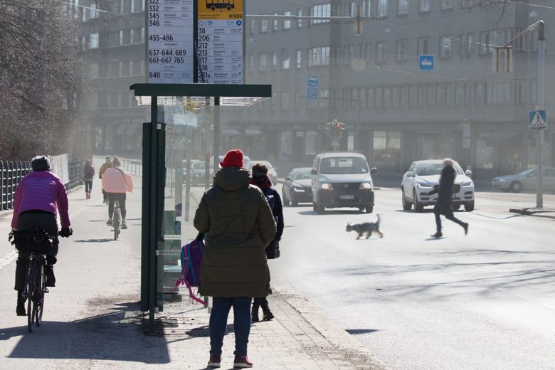Ihmisiä seisoo pysäkillä ja kävelee suojatietä pitkin sankan katupölypilven seassa.