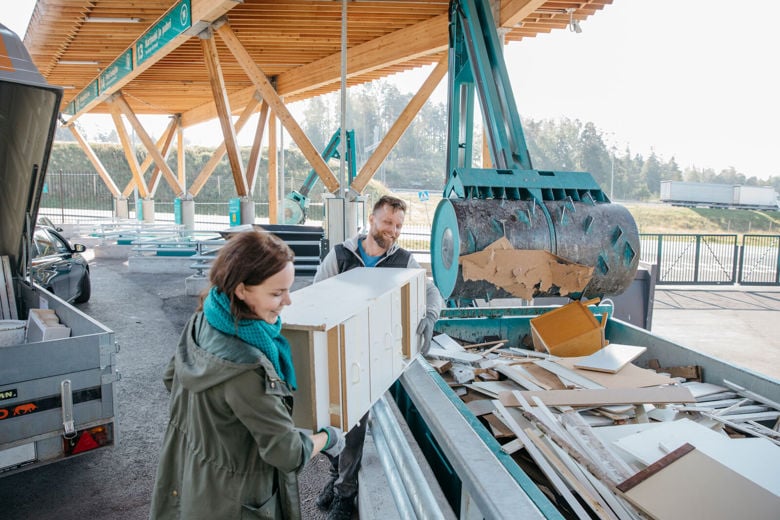 Mies ja nainen nostavat kierrätykseen menevän hyllykön Sortti-asemalla.