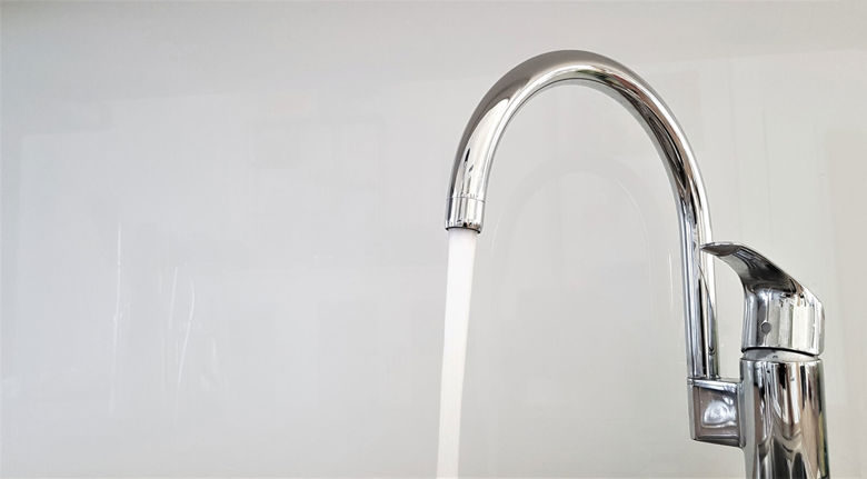 Kuvassa on kiiltävä krominen keittiön vesihana, josta valuu vettä.