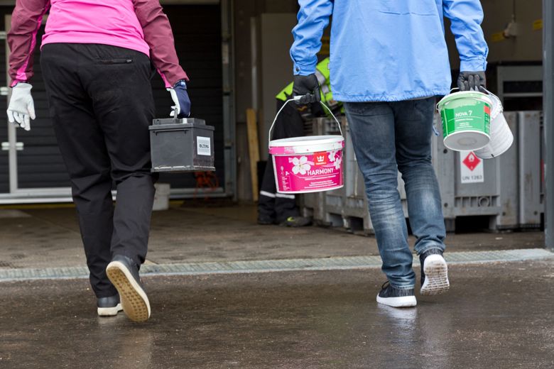  två personer går ifrån kameran och bär farligt avfall i sina händer