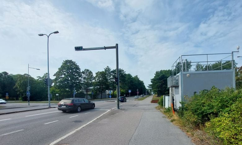 Harmaa ilmanlaadun mittausasema seisoo tien varressa.