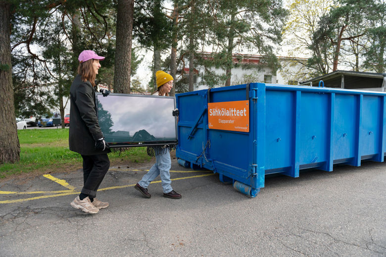 Kaksi asukasta kuljettaa taulutelevisiota Sortti-keräysautokierroksen sähkölaiteromulavalle.