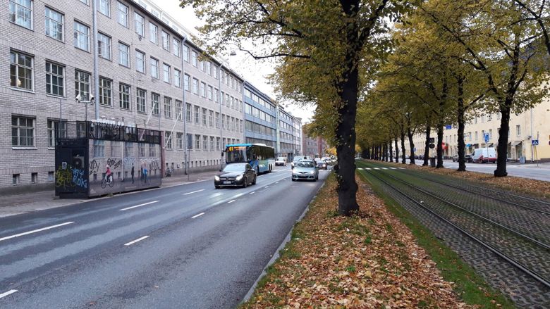 Autoja ja bussi ajavat kadulla ilmanlaadun mittausaseman ohi.