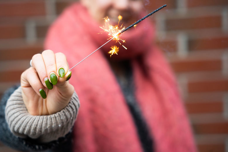 Punaiseen huiviin pukeutunut henkilö pitää kädessään palavaa tähtisadetikkua.