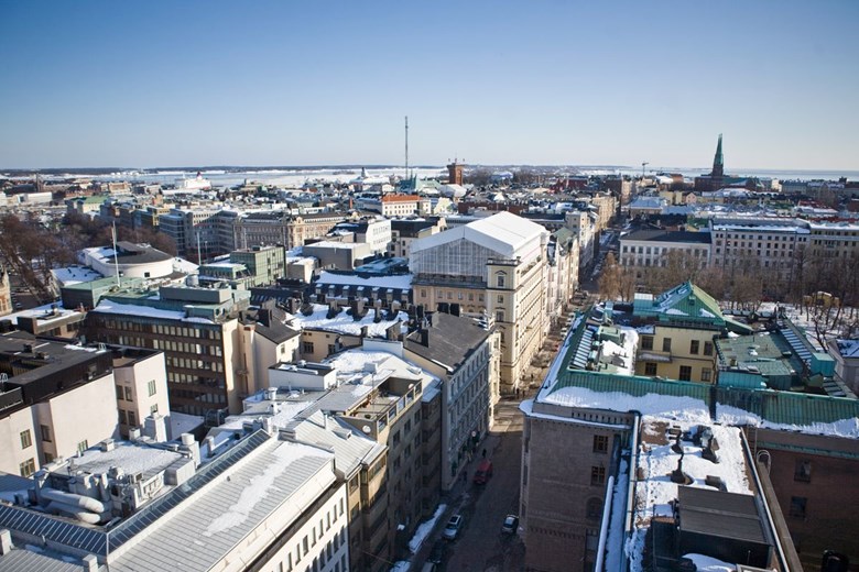 Vintrigt stadslandskap fotograferat från ett tak. Blå himmel, tättstående byggnader och snö på taken.