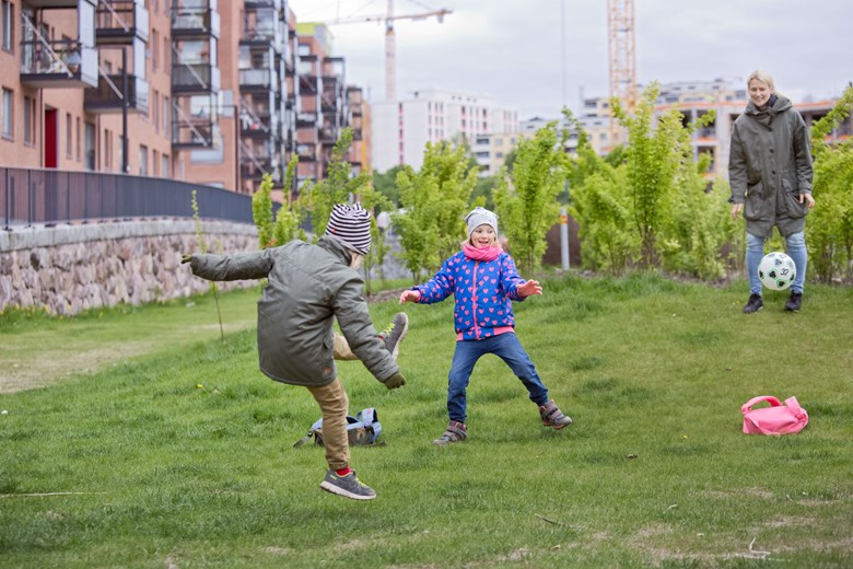 Lapset ja äiti pelaavat jalkapalloa vehressä kaupunkiympäristössä. Kuva: HSY. Kuvaaja: Suvi-Tuuli Kankaanpää.