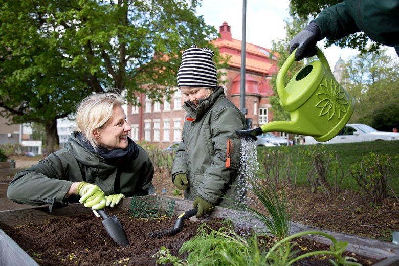 Nainen ja lapsi lapioivat multaa kaupunkivlijelmän äärellä. Kuva: HSY. Kuvaaja: Suvi-Tuuli Kankaanpää.
