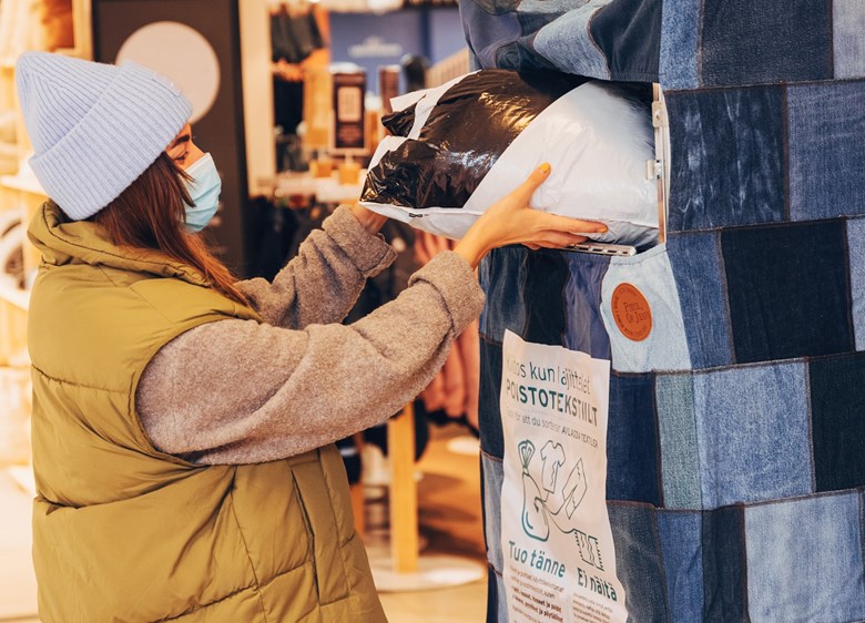 Nainen laittaa poistotekstiilejä sisältävän muovipussin keräysrullakkoon kauppakeskuksessa.