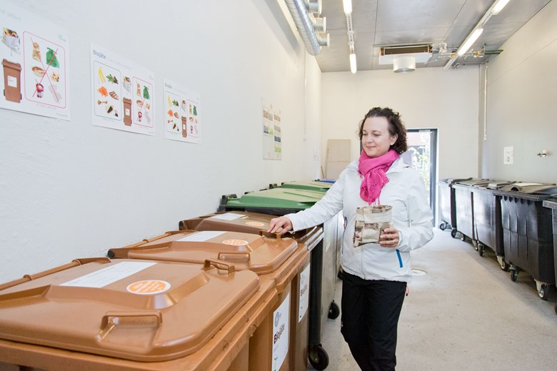 A woman places biowaste in a container in a waste collection room.