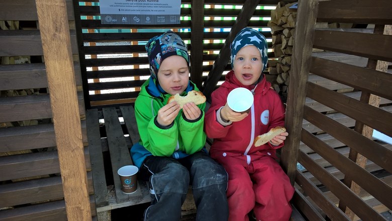 Kaksi lasta syö pullaa puuvajan edustalla.